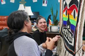 Melina Meyer and Laine Rinehart laugh while weaving the bottom fringe of the Chilkat Pride robe on Saturday. The robe will be exhibited and danced in for the first time during this years Celebration. (Jasz Garrett / Juneau Empire)