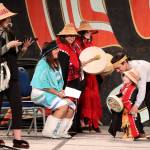 Gyaaaang Peele-Frisby, 2, wears regalia that includes includes a button robe made from the baby blanket of his mother, Sarah Peele, seen at left as she emcees the toddler regalia review as part of Celebration on Thursday at Centennial Hall. (Mark Sabbatini / Juneau Empire)