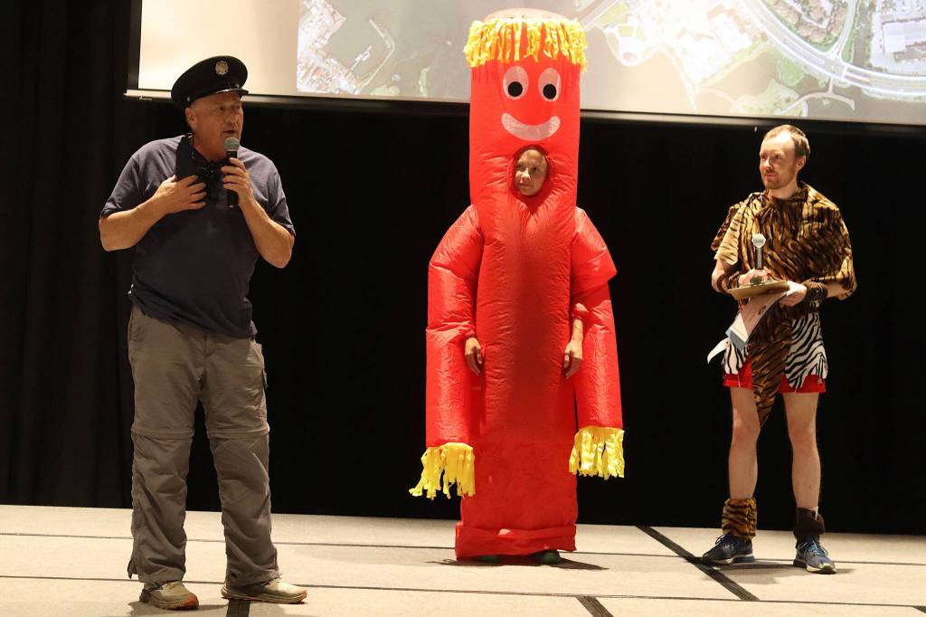 Alan Edwards, left, a retired firefighter who founded the Only Fools Run At Midnight race 40 years ago, talks about the history of the event during the renamed Only Fools Run At Night on Friday at Centennial Hall, as costume clad Abby Jahn, chair of this years race organizing group, and fellow organizer Carl Brodersen listen. (Mark Sabbatini / Juneau Empire)