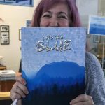 Former Thunder Mountain High School yearbook teacher Janna Lelchuk holds up the 2015-2016 yearbook Into the Blue, which won first place in the American Scholastic Press Associations yearbook competition. (Jasz Garrett / Juneau Empire)