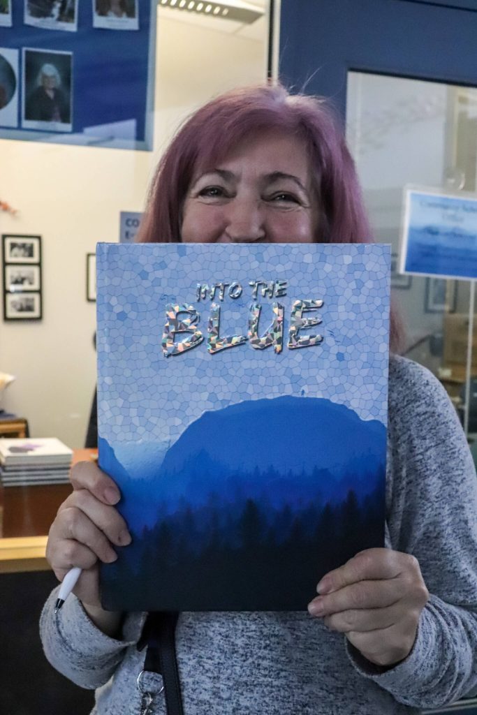 Former Thunder Mountain High School yearbook teacher Janna Lelchuk holds up the 2015-2016 yearbook Into the Blue, which won first place in the American Scholastic Press Associations yearbook competition. (Jasz Garrett / Juneau Empire)