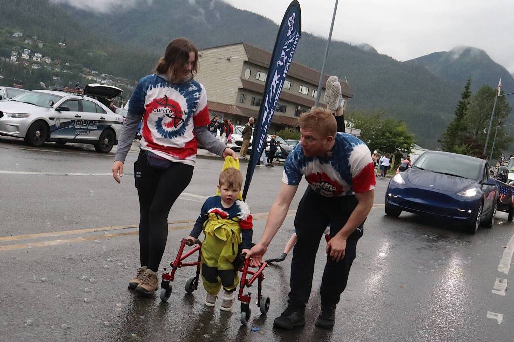 Cade Jobsis, 3, walks with assistance from his parents in Juneaus Fourth of July Parade on Thursday morning. He suffers from a rare genetic disease known as AP-4-associated hereditary spastic paraplegia, and the familys participation in the parade was part of an awareness and fundraising effort. (Mark Sabbatini / Juneau Empire)