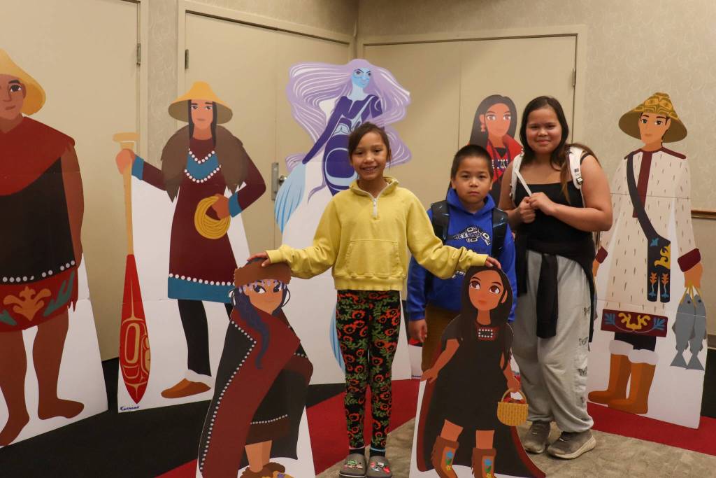Mia Willard, 7, Brandon Lott, 8, and Keisha Lott, 11, stand in front of cardboard cutouts of characters from the Lingít childrens book Kuhaantí at Elizabeth Peratrovich Hall on Saturday.
