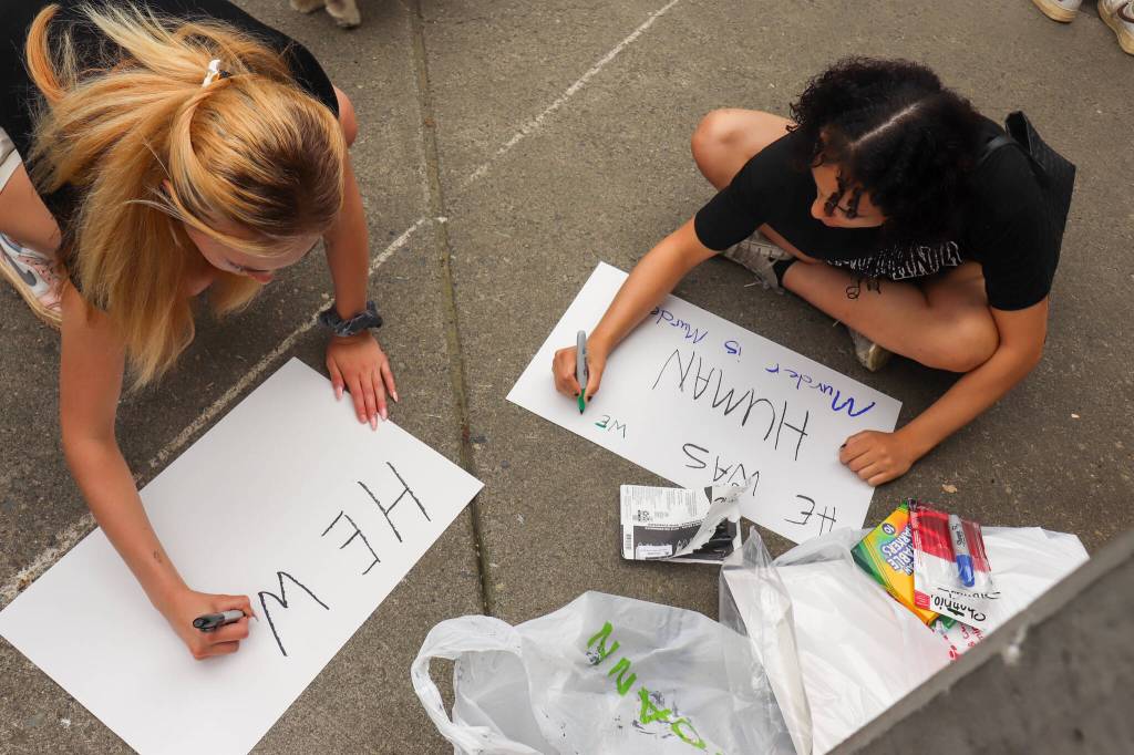 Eulaysia Rayne and Savannah Brohard, organizers of a Sunday protest for Juneau resident Steven Kissack, write signs out front of the Juneau Public Library. (Jasz Garrett / Juneau Empire)