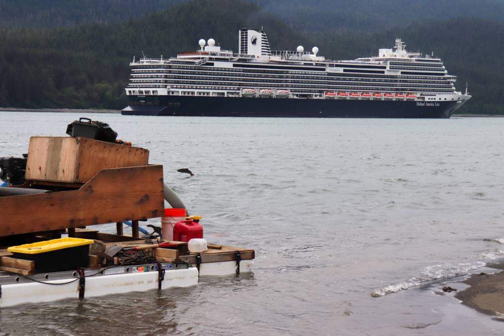 A salmon jumps near a suction dredge on Monday while a cruise ship departs Juneau in Gastineau Channel. (Jasz Garrett / Juneau Empire)