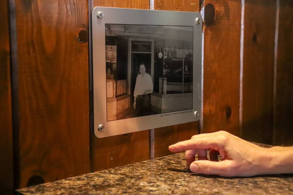 Leeann Thomas, the owner of the Triangle Club for the last 25 years, points at a photo of her grandfather and previous owner, Joe Thomas Sr. (Jasz Garrett / Juneau Empire)