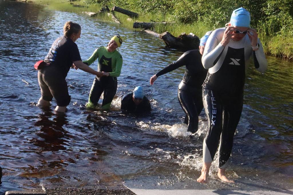 Volunteers help swimmers out of the 62-degree water at Auke Lake during the Aukeman Triathlon on Sunday, (Mark Sabbatini / Juneau Empire)