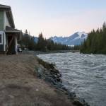 Adam Bishop stands outside his house with friends along the riverbank on Monday evening. (Jasz Garrett / Juneau Empire)