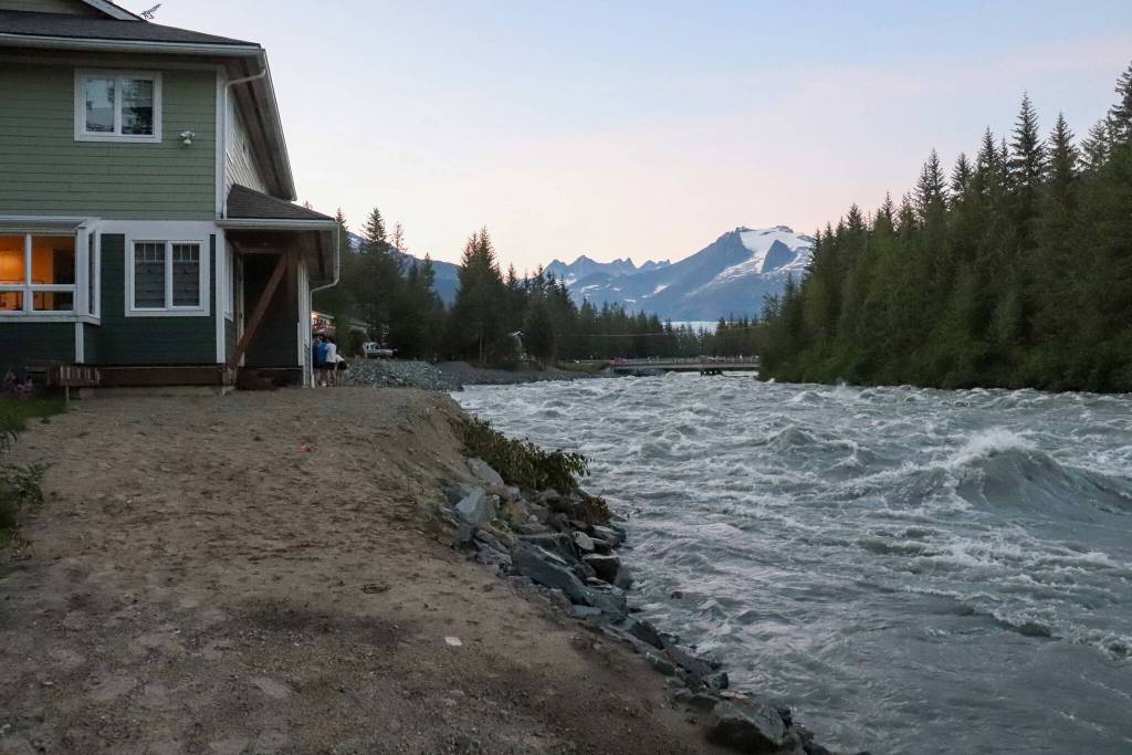 Adam Bishop stands outside his house with friends along the riverbank on Monday evening. (Jasz Garrett / Juneau Empire)