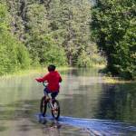 A child rides his bike down the flooded Skaters Cabin Road on Monday afternoon. While the road was closed to vehicles as of midday Monday, it was still open to foot traffic. (Jasz Garrett / Juneau Empire)