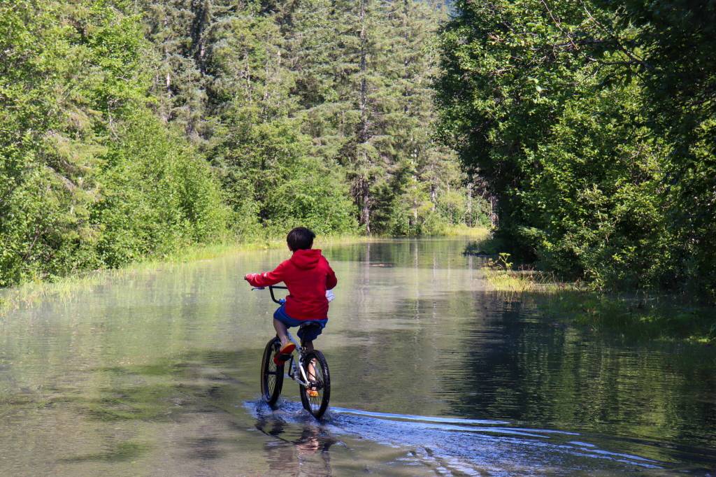 A child rides his bike down the flooded Skaters Cabin Road on Monday afternoon. While the road was closed to vehicles as of midday Monday, it was still open to foot traffic. (Jasz Garrett / Juneau Empire)