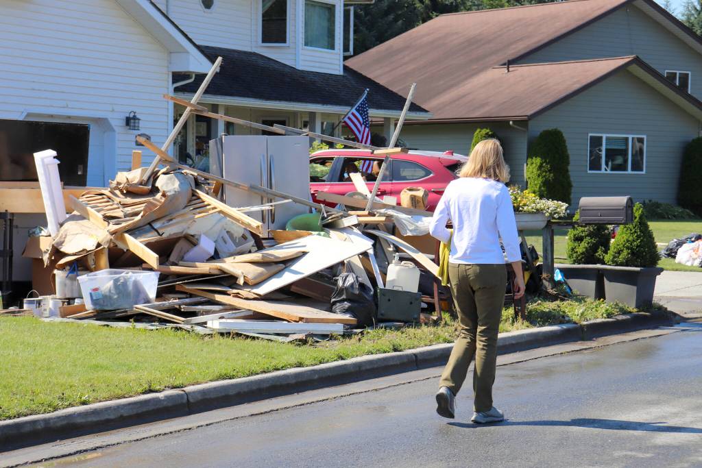 U.S. Sen. Lisa Murkowski walks past a home on Killewich Drive with damaged items left outside in the sun on Wednesday. (Jasz Garrett / Juneau Empire)