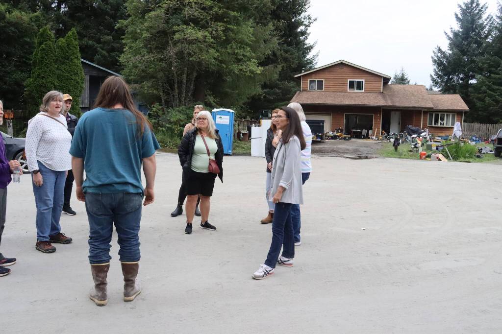 Weston Holland (foreground) explains what happened when the basement of his home in the background was submerged by last weeks record flooding during a visit by officials on Sunday that included U.S. Rep. Mary Peltola (at right). (Mark Sabbatini / Juneau Empire)