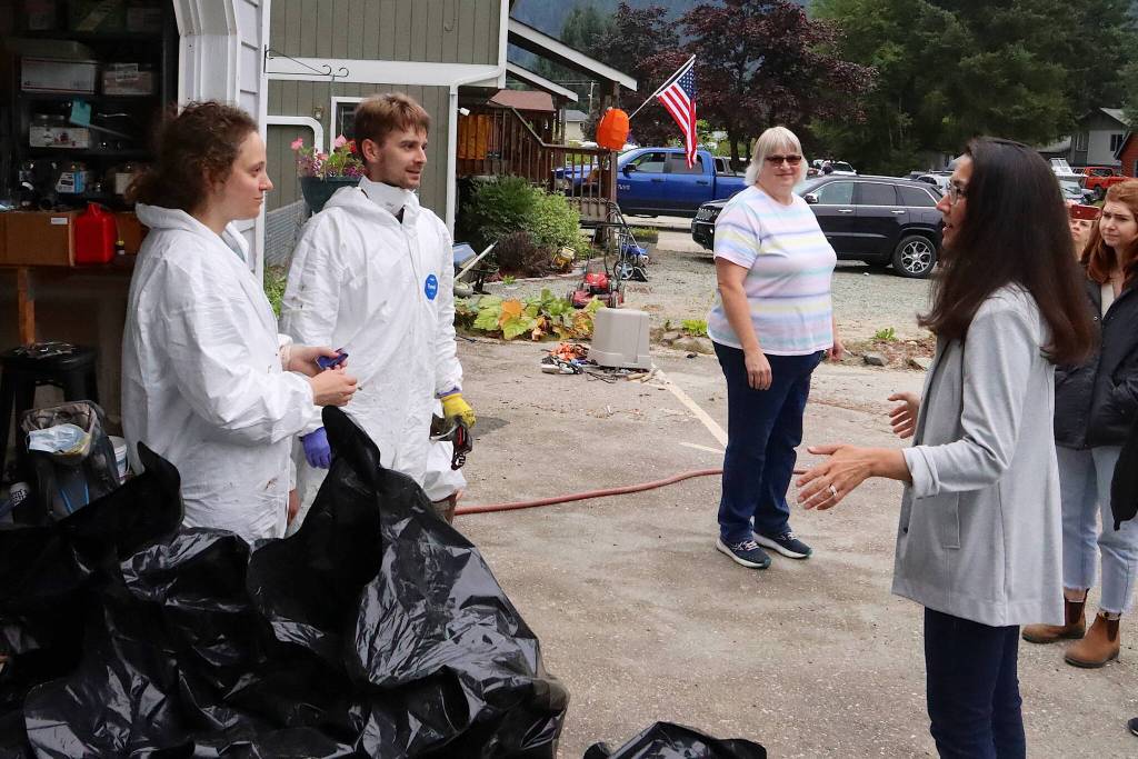 Volunteers Heidi Cope (left) and James Currie wear full-body protective suits as they discuss clearing out insulation and other hazardous material from the flooded crawlspace of a flooded home during a visit Sunday by officials including U.S. Rep. Mary Peltola. (Mark Sabbatini / Juneau Empire)