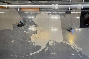 Voters walk across the map of Alaska on the floor of the Alaska State Library, Archives and Museum on Tuesday, Aug. 20, 2024. (James Brooks/Alaska Beacon)