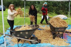 Sigrid Bogert and Fathom Mitchell, both 11, toss straw used during a childrens game into a wheelbarrow to place on a garden plot during the 30th Annual Juneau Community Garden Harvest Fair on Saturday. (Mark Sabbatini / Juneau Empire)