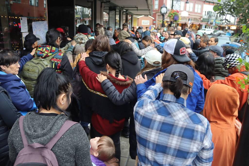 Friends and family of Steven Kissack place their hands on each others shoulders in a show of support at a storefront on Front Street where he often slept during a memorial gathering Sunday. (Mark Sabbatini / Juneau Empire)