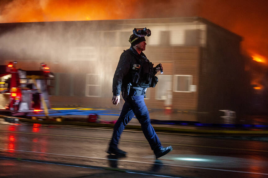 Haines Borough police officer Michael Fullerton helps with crowd control as firefighters battle a fire at the building that houses the Quickshop convenience store, a liquor store, and outdoor store and a handful of apartments on Saturday, Oct. 5, 2024, in Haines. (Rashah McChesney/Chilkat Valley News)