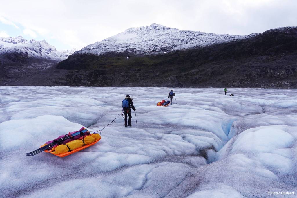 Vincent Colliard, Sarah McNair-Landry and Erik Boomer pull sleds across the Juneau Icefield during their three-week expedition. Along the mountains a strip of bare rock under moss and other foliage shows how the icefield has shrunk in the relatively recent past. (Børge Ousland / Copyright photo used with permission)
