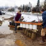 Nathan and Donna Leigh lift a tube loader off a row sandbags after filling them at Melvin Park on Saturday morning. (Mark Sabbatini / Juneau Empire)