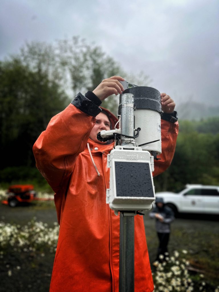 A Prince of Wales Alaska Youth Stewards crew member adjusts tipping bucket and rain gauge on Port Saint Nicholas Road. This device measures rainfall. (Photo by Zofia Danielson)