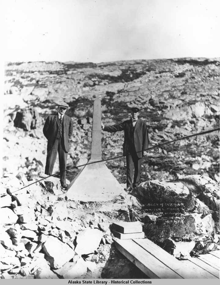 Secretary of Interior Walter Fisher and Alaska Territory Governor Walter Eli Clark (1909-1913) stand beside the boundary monument at White Pass in this undated photo taken near the White Pass and Yukon Route Railway that connects Skagway with Whitehorse, Yukon Territory, Canada. (ASL-P75-317)