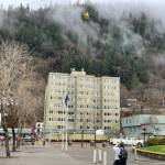 Aurelie Alexander photographs a helicopter hoisting cellular equipment onto the roof of the Marine View building at midday Wednesday. As a resident of the apartment/office building, she and others were notified to leave the building during the helicopter operation. (Laurie Craig / Juneau Empire)