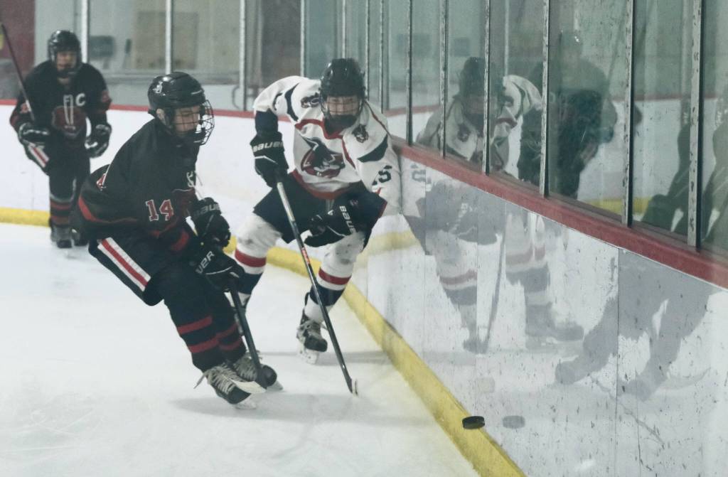 Juneau-Douglas High School: Yadaa.at Kalé freshman Summit Bos (14) works for a puck against North Pole junior Sam Lannet (15) during the Crimson Bears 5-2 loss to the Patriots on Saturday at the Treadwell Ice Arena. (Klas Stolpe / Juneau Empire)