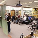 Noah Teshner (right) exhibits the physical impact military-grade flood barriers will have on properties with the help of other residents at a Juneau Assembly meeting on Monday night. (Mark Sabbatini / Juneau Empire)