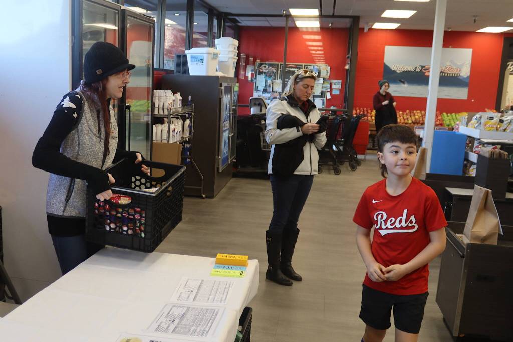 Kelly Moore (left), a board member of the Southeast Alaska Food Bank, accepts a crate of donated food from Kalon Herman, 9, at Super Bear IGA on Saturday morning as part of the food banks annual Caring is Sharing Food Drive. (Mark Sabbatini / Juneau Empire)