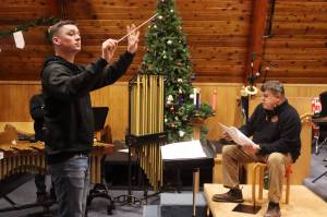 Alan Young (left) conducts while John Cooper reads the words to The Night Before Christmas during a rehearsal Wednesday for holiday concerts by the Taku Winds brass ensemble at K̠unéix̠ Hídi Northern Light United Church. (Mark Sabbatini / Juneau Empire)