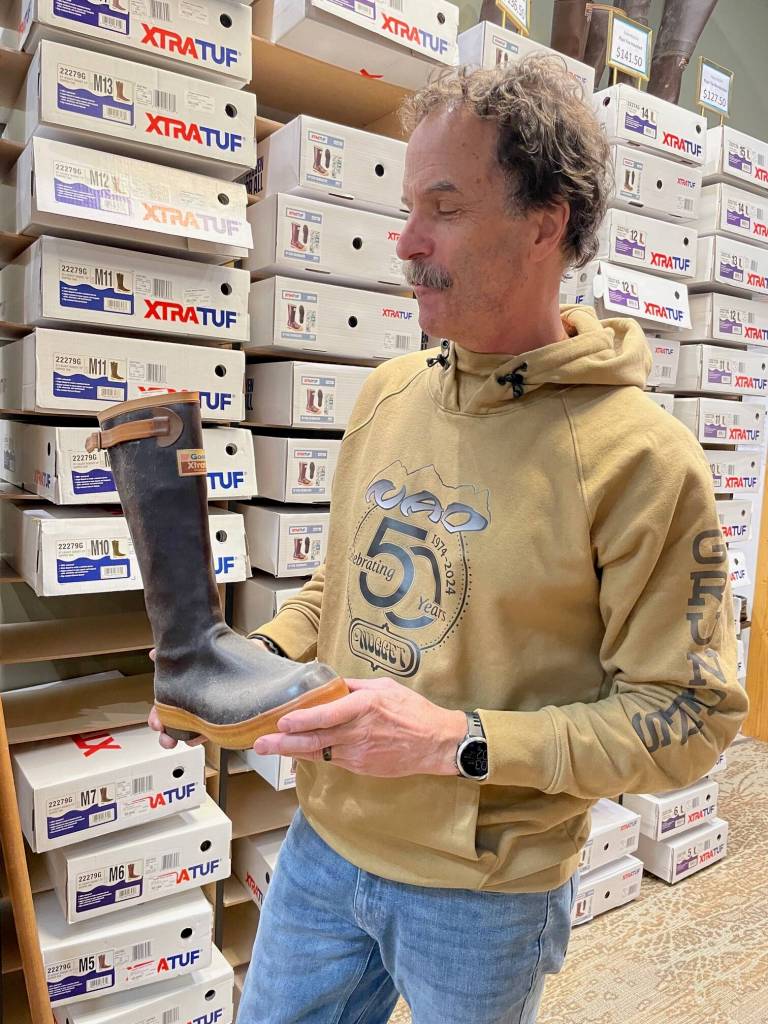 Ron Flint holding a forerunner rubber boot with the BF Goodrich name above XtraTuf logo on the boot front. (Laurie Craig / Juneau Empire)