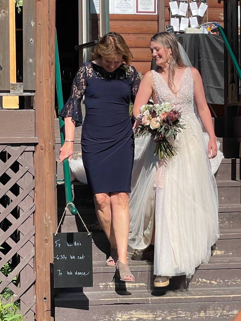 Carly Craig, raised in Juneau, wears XtraTuf rubber boots with her long gown on her wedding day in Seward in June of 2022. Her mother JoAnne Craig escorts her daughter to the altar in an outdoor ceremony surrounded by friends and family, including the author. (Laurie Craig / Juneau Empire)