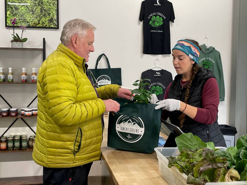Retired chef Kirk Stagg picks up a bag of fresh edible greens from Amy White at Juneau Greens new storefront. (Laurie Craig / Juneau Empire)