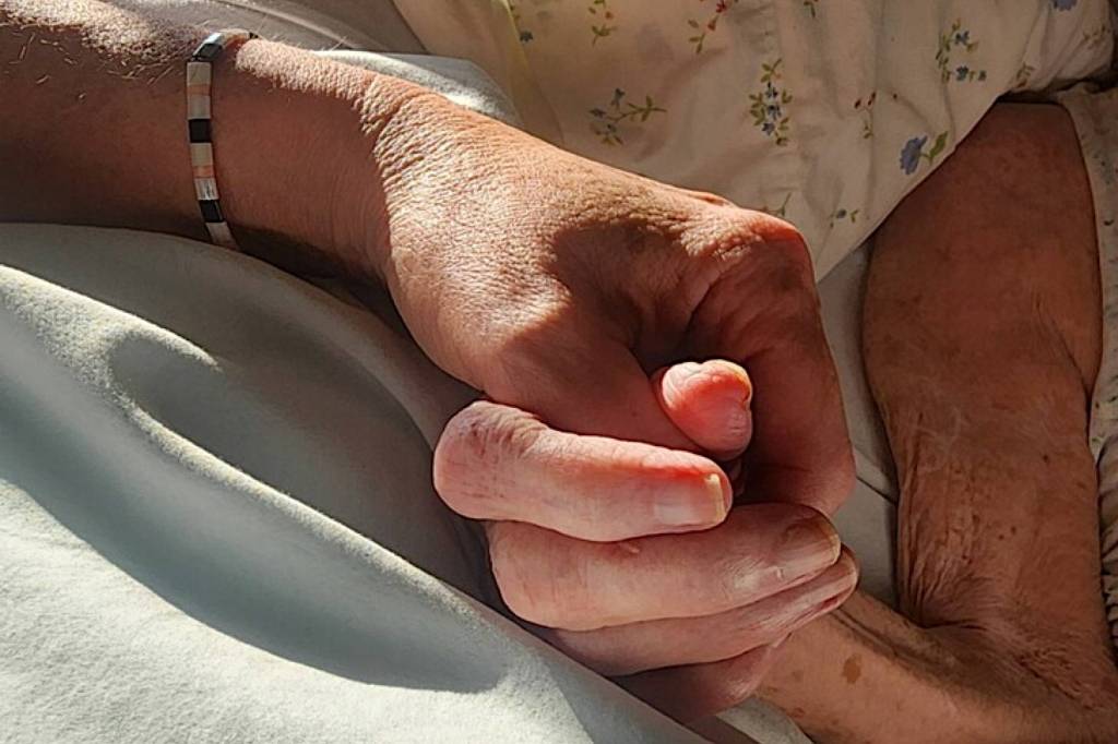 The author holds her mothers hand two hours before she died. (Photo by Gabriella Hebert)