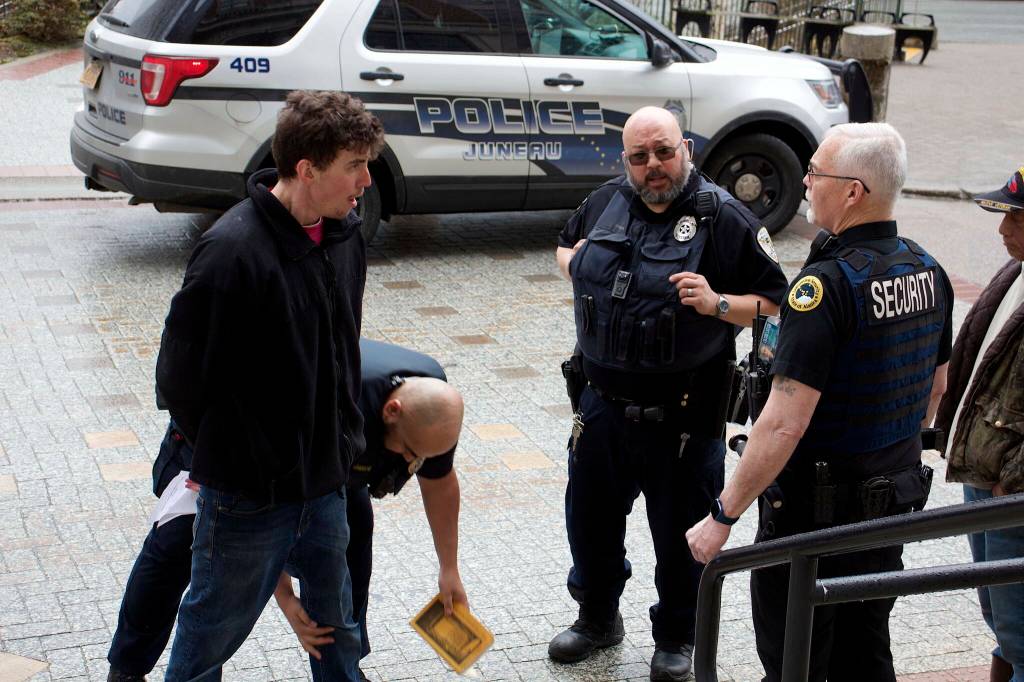 A man is searched by a Juneau Police Department officer as he arrested April 17 after causing disturbances at the Alaska State Capitol and State Office Building. (Mark Sabbatini / Juneau Empire file photo)