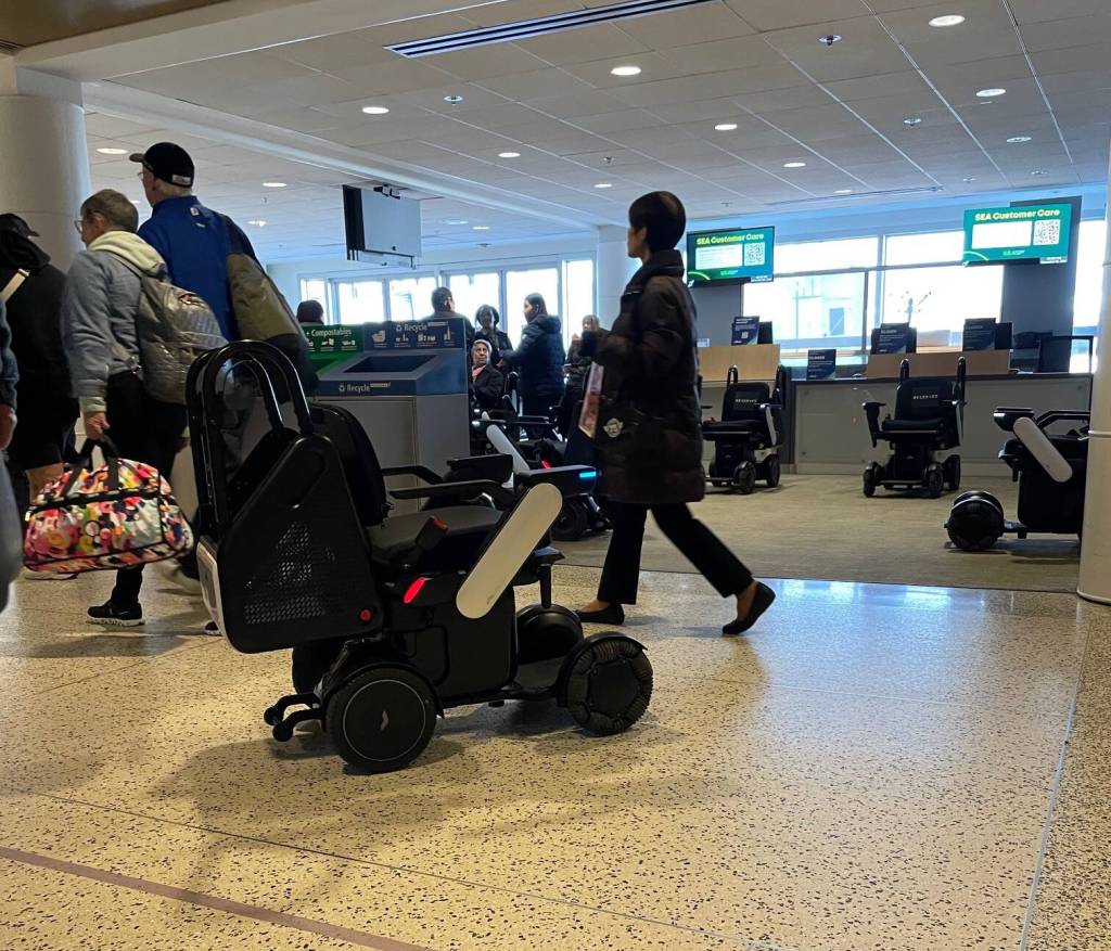 An unoccupied autonomous motorized wheelchair manufactured by Whill pauses for pedestrian traffic before turning into its parking station in D Concourse on Dec. 3 at Seattle–Tacoma International Airport. (Laurie Craig / Juneau Empire)