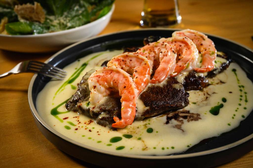 Steak with prawns and shrimp scampi sauce at Bocca al Lupo, which has an industrial atmosphere, in Juneau, Alaska, June 2, 2024. The states capital, a popular cruise port in summer, becomes a bargain-seekers base for skiing, skating, hiking and glacier-gazing in the winter off-season. (Christopher S. Miller/The New York Times)