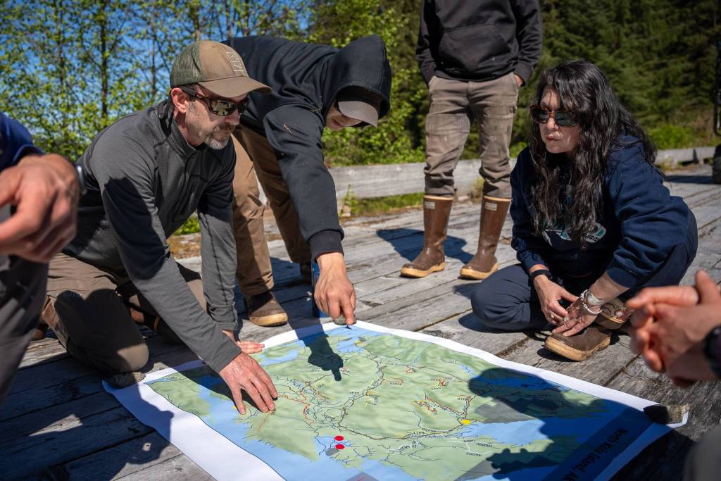 Left to right: Heath Whitacre (U.S. Forest Service), Jason Gubatayao (Sealaska), Khaax̱wáan Dawn Jackson (Organized Village of Kake) sit on the bridge over Yeíl Héeni (Ravens Creek) discussing points on a map of north Kuiu Island. (Photo by Lee House)