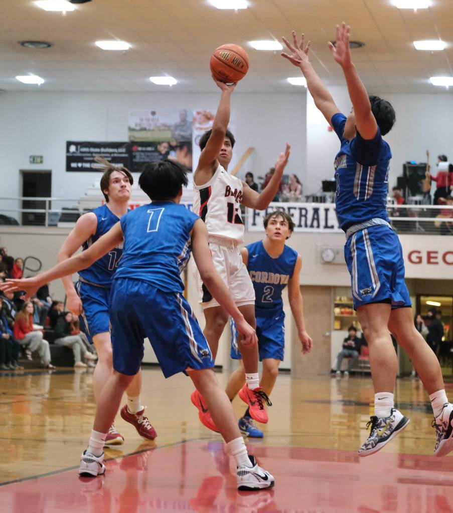 Juneau-Douglas High School: Yadaa.at Kalé junior Joren Gasga (12) floats in a shot over Cordova seniors John Itliong (1) and Chiko Jacob (24) during the Crimson Bears 62-39 win over the Wolverines in the nightcap game of the opening day of the George Houston Capital City Classic on Friday in Juneau. (Klas Stolpe / Juneau Empire)