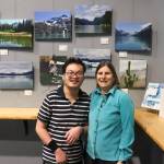 Fu Bao Hartle stands next to his mom with his artwork behind them on Thursday. He thanked his mom for her help in running his business. (Jasz Garrett / Juneau Empire)