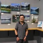 Fu Bao Hartle stands with his first solo photography exhibit at the Alaskan Brewery Tasting room on Thursday. (Jasz Garrett / Juneau Empire)