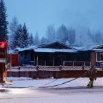 A firefighter carries a hose toward a Mendenhall Valley house still experiencing flareups hours after a fire started early Saturday morning. (Mark Sabbatini / Juneau Empire)