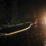 A firefighter rolls up a hose in the rain after completing a fire response at Sprucewood Park. (Jasz Garrett / Juneau Empire)
