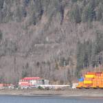 Ruins of the Alaska-Juneau Gold Mine mill are visible through leafless trees above the red roofed steam plant near Alaska Marine Lines containers stacked at the rock dump in this April 3, 2024, photo taken from Douglas Island. (Laurie Craig / Juneau Empire)