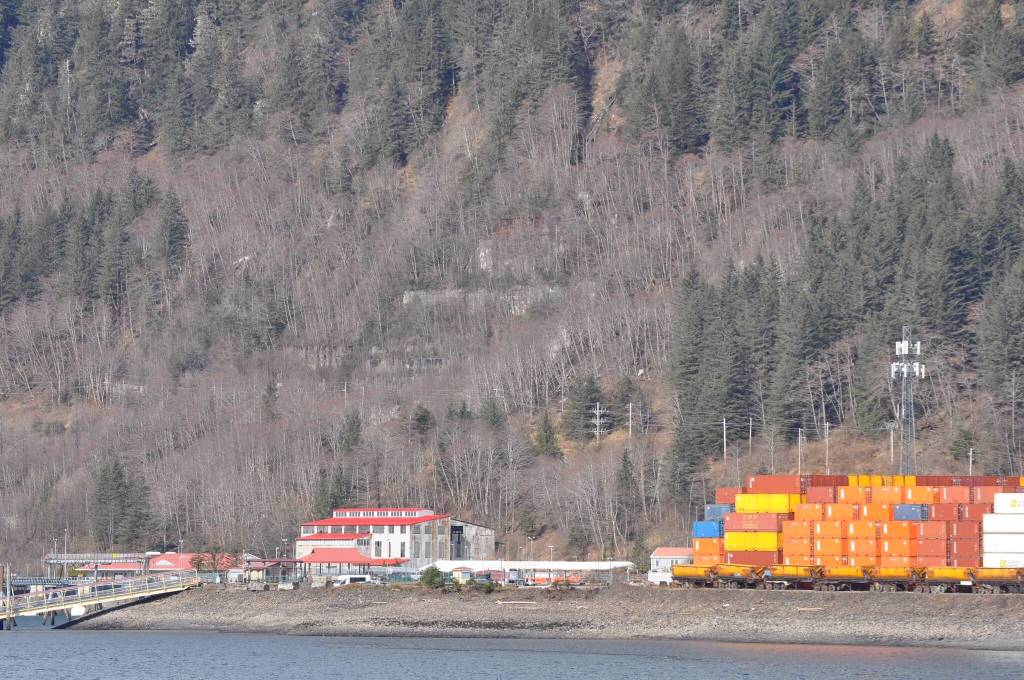 Ruins of the Alaska-Juneau Gold Mine mill are visible through leafless trees above the red roofed steam plant near Alaska Marine Lines containers stacked at the rock dump in this April 3, 2024, photo taken from Douglas Island. (Laurie Craig / Juneau Empire)