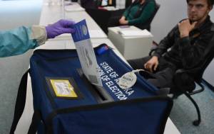 A voter in Alaskas special U.S. House primary election drops their ballot into a box on Saturday, June 11, 2022 as a poll worker observes. (James Brooks/Alaska Beacon)