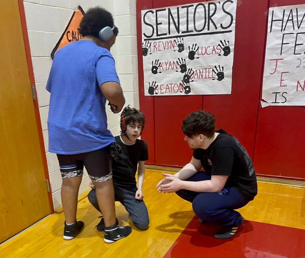 Thunder Mountain Middle School heavyweights Braedon-Lee Atrim and Barron Marexo help first-year wrestler Tanner Freebury prepare for his match in Wrangell Saturday. (Photo courtesy TMMS)