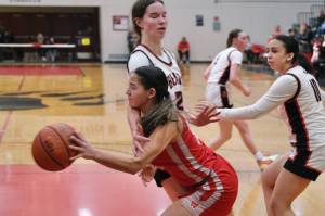 Wasilla junior Katie Jackson drives and passes around Juneau-Douglas High School: Yadaa.at Kalé seniors Cailynn Baxter and Addison Wilson (10) during the Warriors 65-34 win Friday over the Crimson Bears in the George Houston Gymnasium. (Klas Stolpe / Juneau Empire)