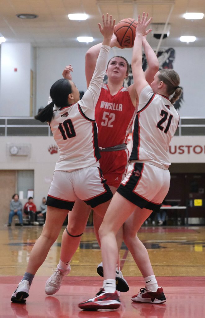 Wasilla senior Layla Hays (52) scores over Juneau-Douglas High School: Yadaa.at Kalé senior Addison Wilson (10) and freshman Athena Warr (21) during the Warriors 65-34 win over the Crimson Bears on Friday in the George Houston Gymnasium. (Klas Stolpe / Juneau Empire)